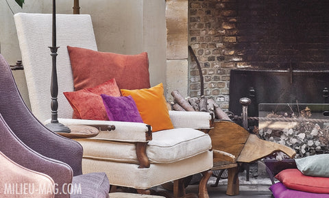 Los cojines color frambuesa con violeta y mandarina aportan color y calidez al antiguo sillón junto al fuego - Walda Pairon