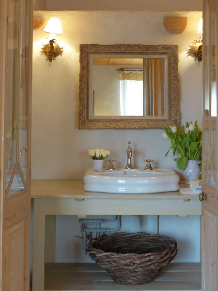 Canasta tejida francesa debajo del lavabo del baño con espejo antiguo